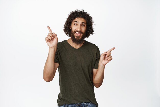 Chico guapo sonriente señalando con el dedo hacia los lados mostrando el gesto izquierdo y derecho dos opciones de pie sobre fondo blanco.