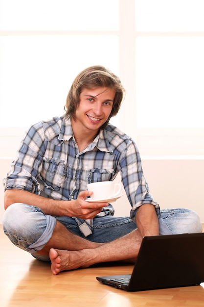 Chico guapo con una taza de café y una computadora portátil