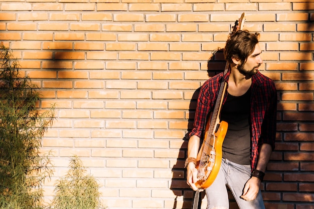 Chico con guitarra eléctrica junto a muro de ladrillo