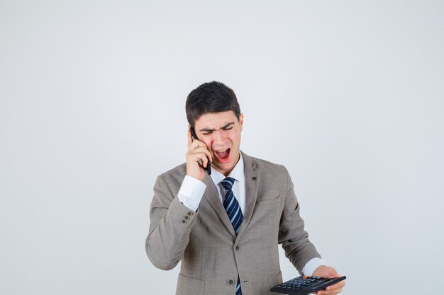 Chico hablando por teléfono, sosteniendo la calculadora en traje formal