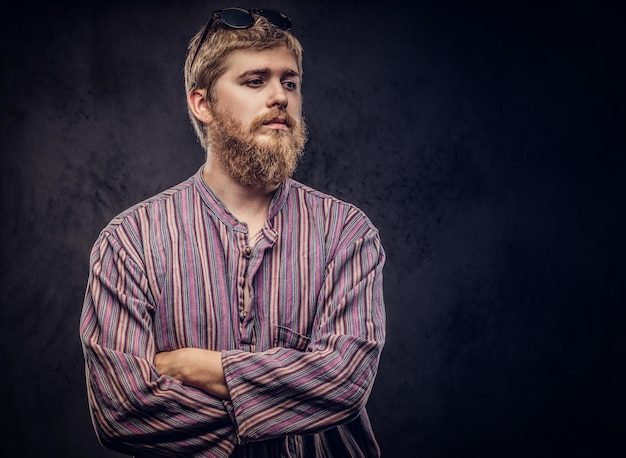 Chico hipster barbudo pelirrojo vestido con una camisa anticuada de pie con los brazos cruzados. Aislado en un fondo oscuro.