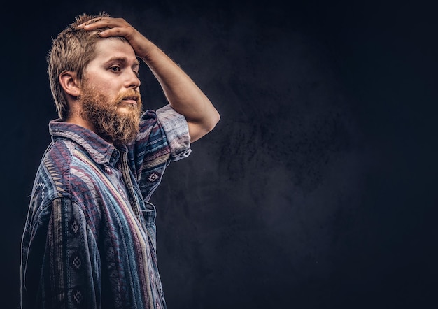 Foto gratuita chico hipster barbudo pelirrojo vestido con una camisa pasada de moda posando con la mano en la cabeza. aislado en un fondo oscuro.