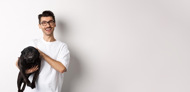 Foto gratuita chico hipster feliz con gafas, perro mascota y pug negro lindo y sonriente, disfrutan pasar tiempo con el dueño looki