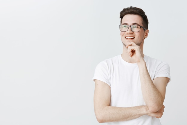 Chico inteligente pensativo con gafas mirando complacido a la izquierda, sonriendo de buena idea