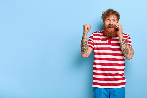 Chico jengibre con estilo feliz lleno de alegría posando contra la pared azul