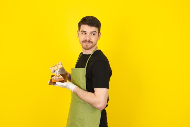 Un chico joven atractivo que sostiene pasteles caseros frescos en amarillo.