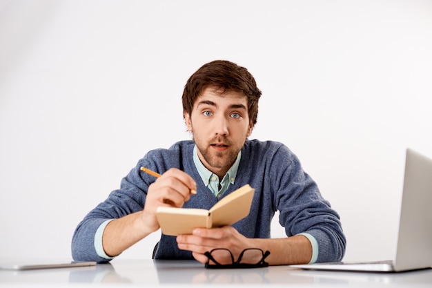 Chico joven con barba interesado, aprende cursos de idiomas nuevos en línea mientras te sientas en casa en cuarentena, escribes en un cuaderno, pareces interesado