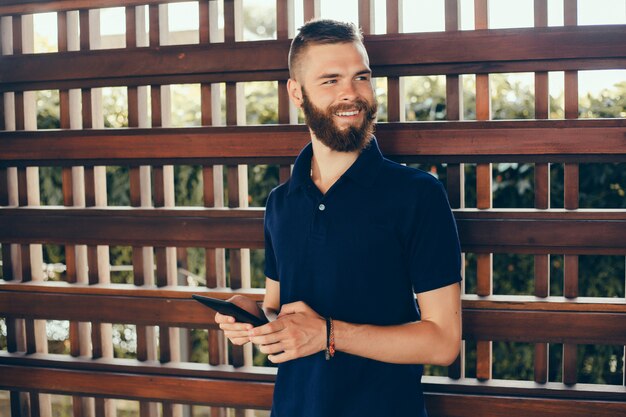 un chico joven con barba trabaja en un café, un profesional independiente usa una tableta, hace un proyecto