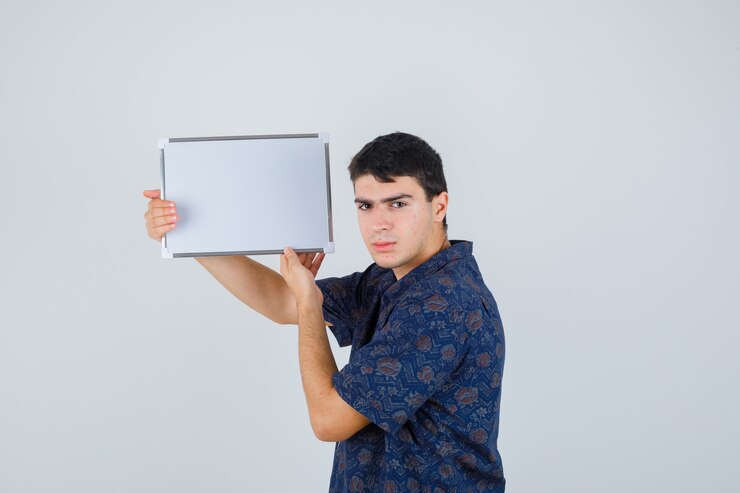 Foto gratuito chico joven en camisa floral sosteniendo pizarra y mirando serio