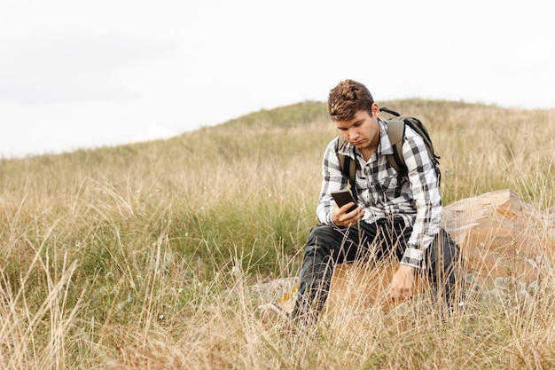 Foto gratuita chico joven chequeando su teléfono en la naturaleza salvaje