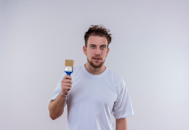 Chico joven contento con camiseta blanca sosteniendo pincel sobre fondo blanco aislado