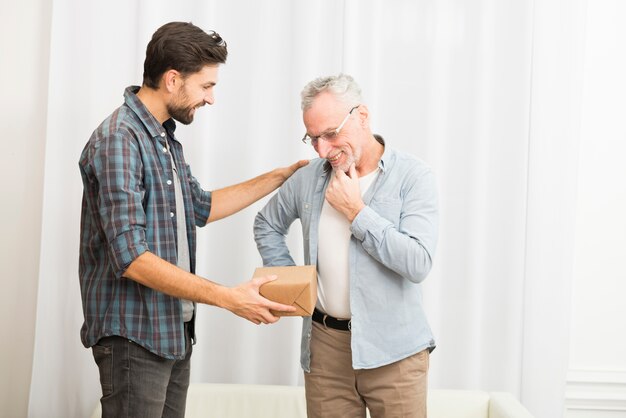 Chico joven dando presente a anciano hombre feliz.