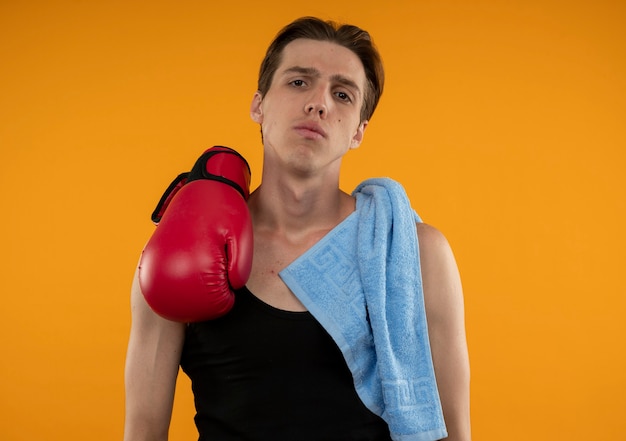 Chico joven deportivo con toalla y guantes de boxeo en el hombro aislado en la pared naranja
