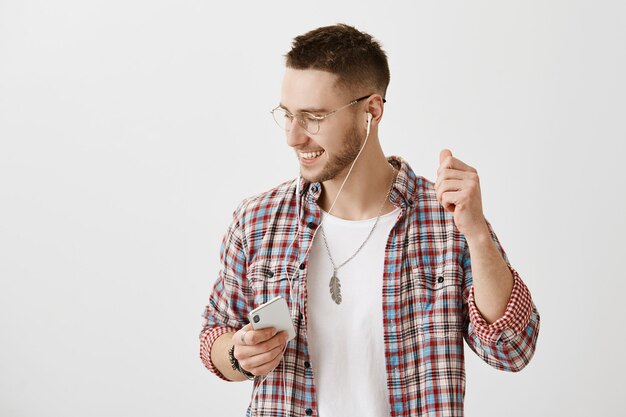 Chico joven despreocupado con gafas posando con su teléfono y auriculares