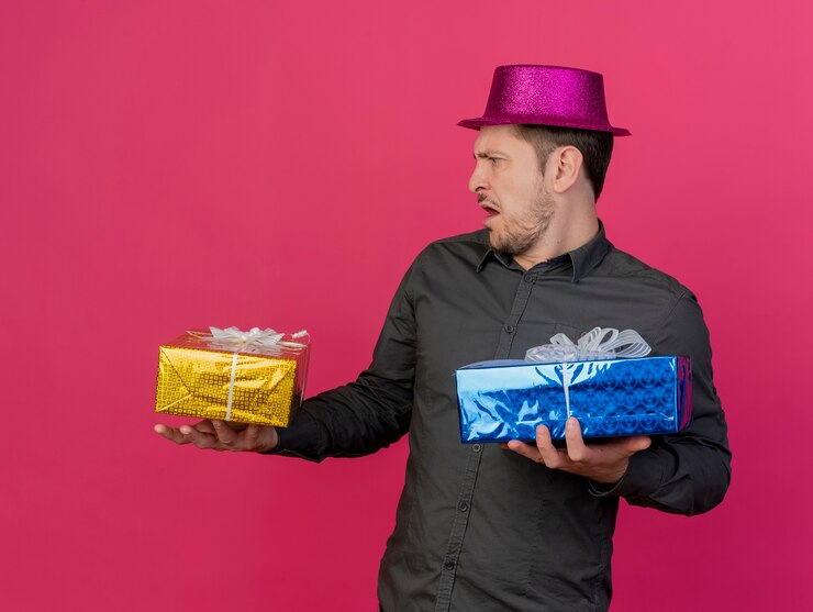 Foto gratuito chico joven disgustado con sombrero rosa sosteniendo una caja de regalo en el lado aislado en rosa