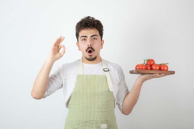 Chico joven emocionado sosteniendo un montón de tomates frescos y gesticulando bien. .