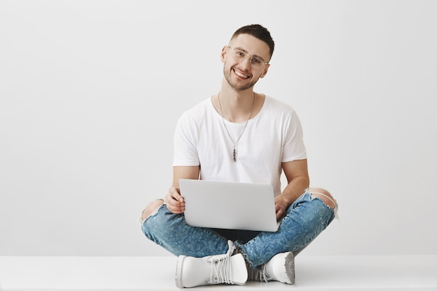 Foto gratuita chico joven guapo con gafas posando con su computadora portátil