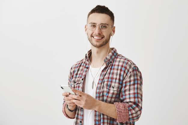 Chico joven guapo con gafas posando con su teléfono y auriculares