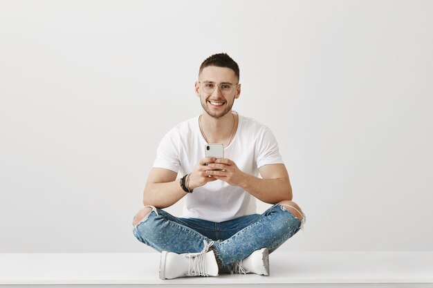 Foto gratuita chico joven guapo con gafas posando con su teléfono