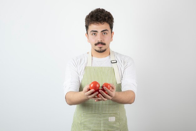 Chico joven guapo sosteniendo tomates orgánicos y mirando directamente a la cámara.