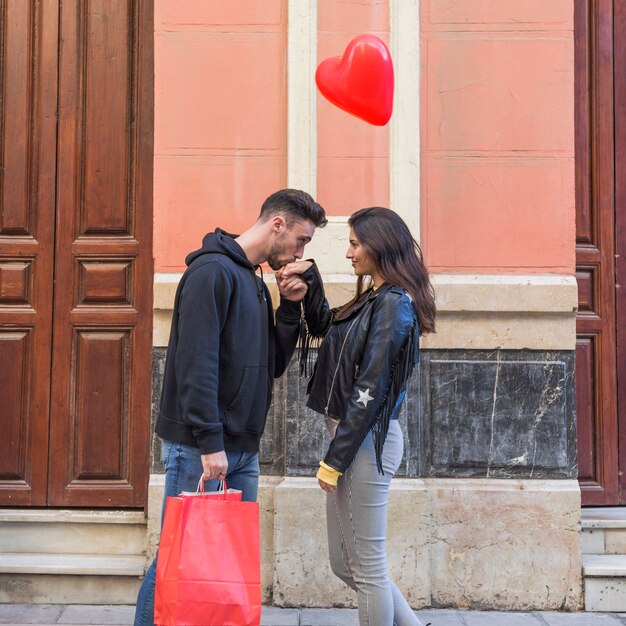 Chico joven con paquetes que besan la mano de una dama y un globo volador