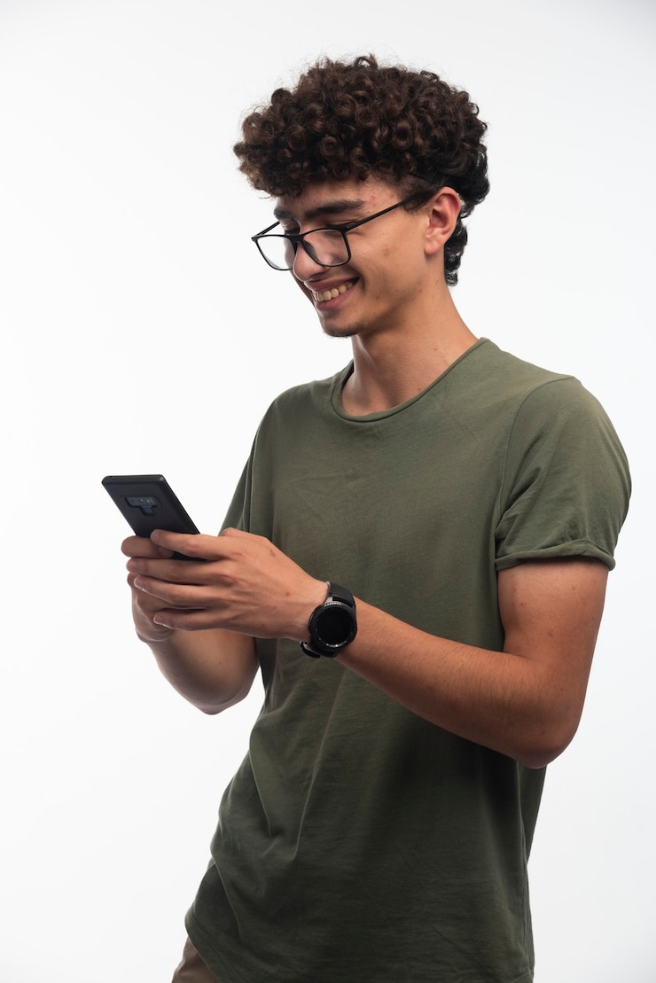 Foto gratuito chico joven con pelos rizados revisando mensajes y se pone feliz.