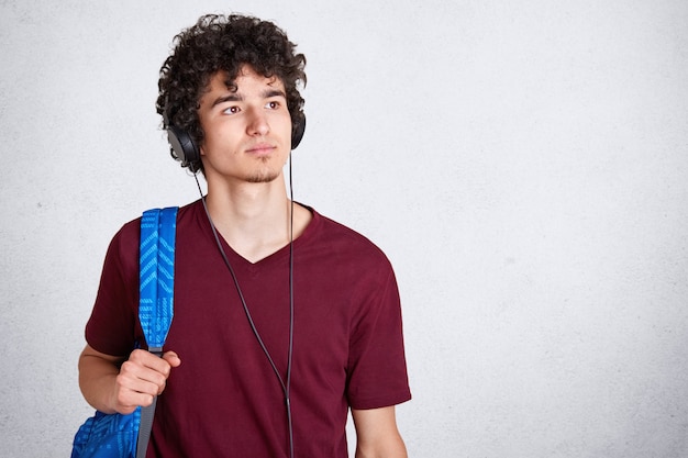 Foto gratuita chico joven pensativo con auriculares en la cabeza y mochila azul