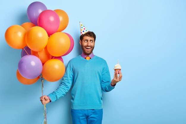 Chico joven con sombrero de cumpleaños y globos posando en suéter azul