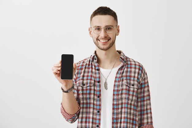 Chico joven sonriente guapo con gafas posando con su teléfono