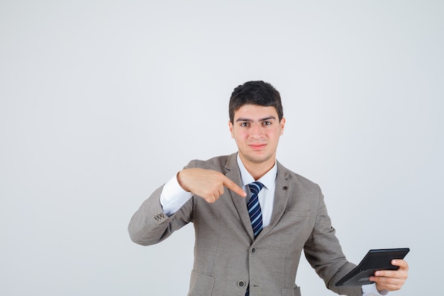 Chico joven en traje formal sosteniendo la calculadora, apuntando a ella