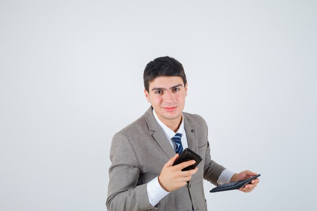 Chico joven en traje formal sosteniendo teléfono y calculadora