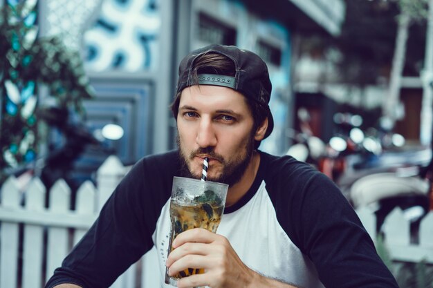 Chico joven usa un teléfono inteligente en una cafetería, navega por Internet, mira videos, bebe