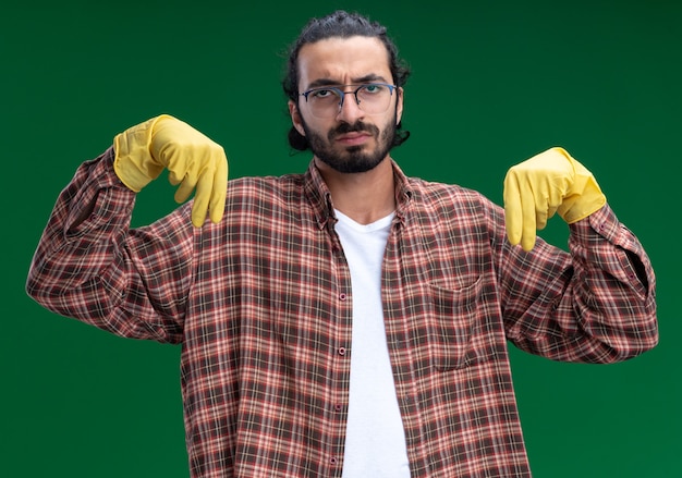 Foto gratuita chico de limpieza guapo joven disgustado con camiseta y guantes fingiendo sostener algo aislado en la pared verde