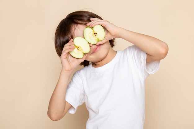 Foto gratuita chico lindo adorable sosteniendo medio corte manzana verde en escritorio rosa