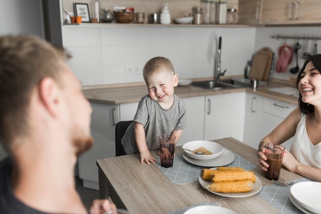 Chico lindo disfrutando el desayuno con sus padres en la cocina.