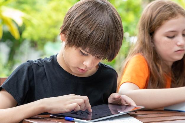 Chico lindo usando tableta mientras hace la tarea con su hermana en el jardín en casa