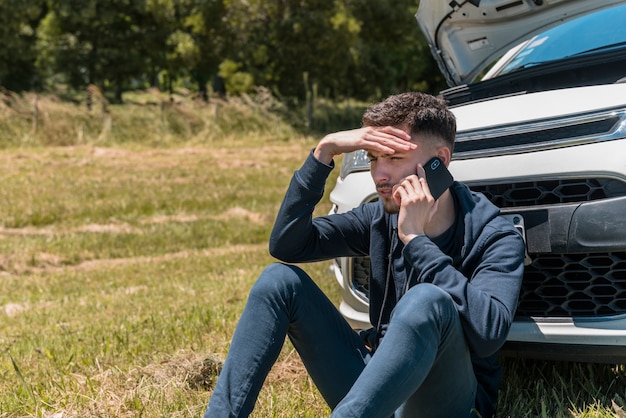 Chico llamando junto a coche averiado