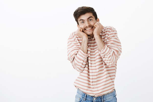 Foto gratuita chico maduro feliz como un niño. retrato de interior de un emotivo modelo masculino europeo feliz con expresión linda, tomados de la mano en las mejillas e inclinando la cabeza, sonriendo positivamente al ver un adorable cachorro