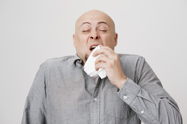Chico de mediana edad calvo enfermo estornudando en la servilleta