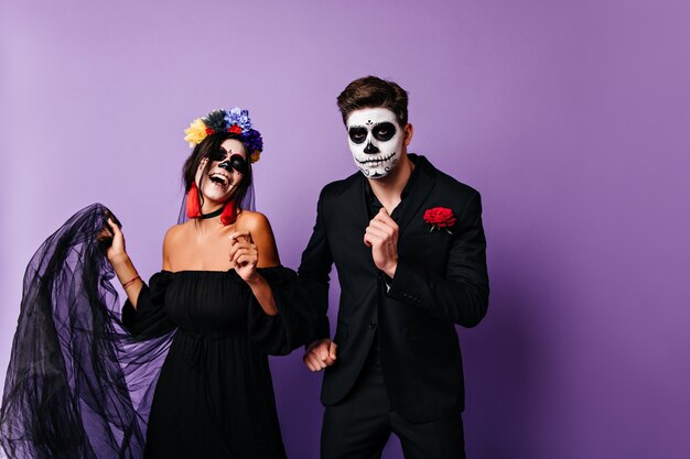 Chico mexicano seguro bailando con novia en el día de los muertos. Pareja casada celebrando halloween en disfraces.