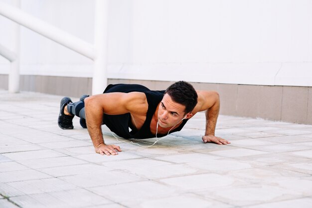 Chico musculoso atractivo haciendo ejercicios de flexiones de brazos, durante el entrenamiento al aire libre