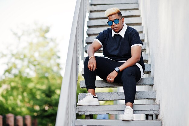 Chico musulmán árabe elegante con cabello original y gafas de sol posadas en las calles en la escalera