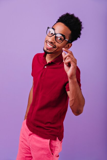 Chico negro entusiasta posando con sonrisa feliz. joven africano inspirado en gafas de moda.