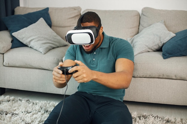 Chico negro con gafas de realidad virtual sentado en una alfombra en la sala de estar