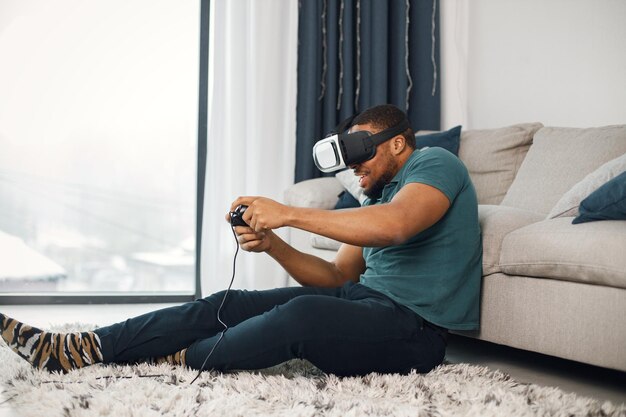 Chico negro con gafas de realidad virtual sentado en una alfombra en la sala de estar