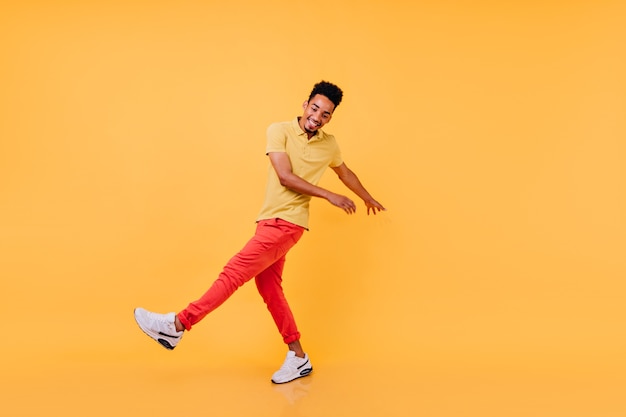 Chico negro inspirado en el baile divertido traje casual brillante. Riendo modelo masculino africano en camiseta amarilla y pantalón rojo bromeando.