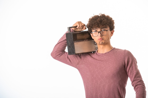 Chico de pelo rizado con gafas ópticas sosteniendo una radio vintage y parece decepcionado.