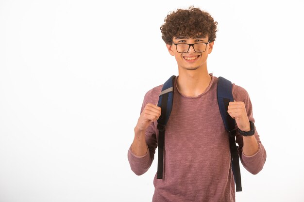 Chico de pelo rizado en gafas ópticas sosteniendo su mochila y está listo para viajar.