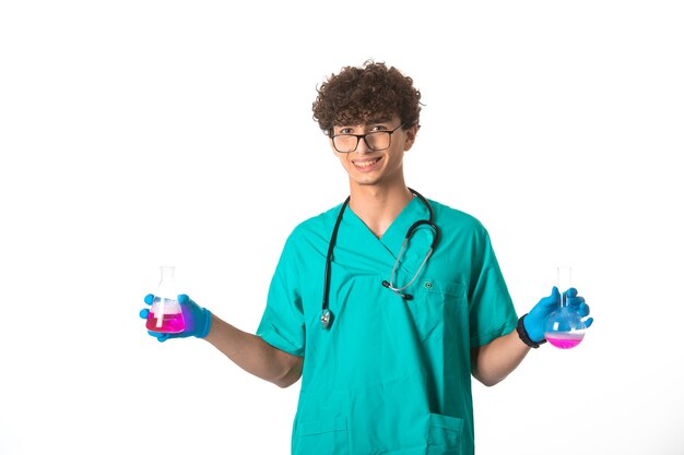 Chico de pelo rizado en uniforme médico y máscaras de mano comprobando las pruebas y luciendo exitoso.