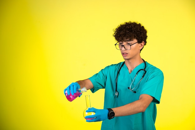 Chico de pelo rizado en uniforme médico y máscaras de mano haciendo reacción con líquido químico.